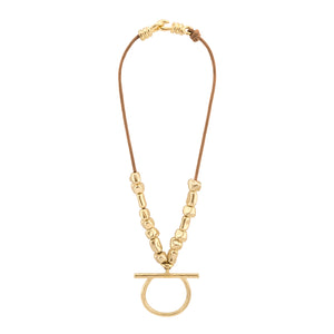 Collar de cordón color camel con cuentas doradas de forma irregular, con un colgante central en forma de aro y barra horizontal. El collar se cierra con un broche de gancho dorado, complementando el diseño minimalista y elegante.
