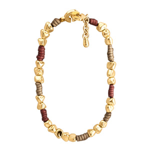 Pulsera de diseño moderno que combina cuentas doradas irregulares con secciones de cuero color taupe y rojo tinto. Las cuentas doradas tienen formas únicas y facetadas, dando un aspecto orgánico y artesanal. El cuero color taupe y rojo tinto está dispuesto en pequeñas secciones entre grupos de cuentas doradas. La pulsera tiene un cierre circular dorado con un diseño distintivo y grabado con el texto "CORSO". Una pequeña cadena dorada cuelga del cierre, probablemente para ajustar el tamaño. El contraste entr