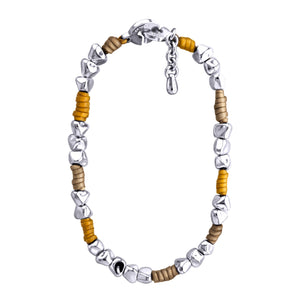 Pulsera de diseño moderno que combina cuentas de plata irregulares con secciones de cuero color taupe y mostaza. Las cuentas plateadas tienen formas únicas y facetadas, dando un aspecto orgánico y artesanal. El cuero color taupe y mostaza está dispuesto en pequeñas secciones entre grupos de cuentas plateadas. La pulsera tiene un cierre circular plateado con un diseño distintivo. Una pequeña cadena plateada cuelga del cierre, probablemente para ajustar el tamaño. El contraste entre la plata brillante y el cu