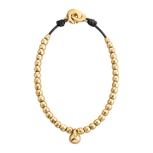 Una imagen de un collar elegante compuesto por esferas doradas uniformes, color dorado, enhebradas en un cordón negro. En el centro del collar cuelga un pequeño dije o colgante también dorado con forma redondeada. El cierre del collar es una pieza circular dorada con un diseño distintivo, conectada al cordón negro en ambos extremos. Este collar combina el brillo del metal precioso con la textura oscura del cordón, creando un contraste atractivo y sofisticado.