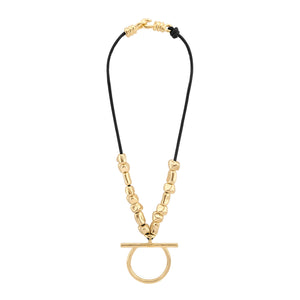 Collar de cordón negro con cuentas doradas de forma irregular, con un colgante central en forma de aro y barra horizontal. El collar se cierra con un broche de gancho dorado, complementando el diseño minimalista y elegante.