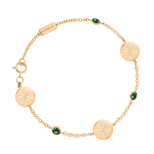 Elegante pulsera de oro de cadena fina, adornada con tres colgantes circulares. Cada colgante presenta un intrincado grabado de un trébol de cuatro hojas. Entre los colgantes, se encuentran engastadas tres esmeraldas verdes ovaladas que añaden un toque de color y sofisticación.