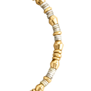 Detalle de pulsera con cuentas doradas y plateadas de diferentes formas y tamaños, unidas por un cordón claro.