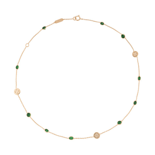 Collar de oro con piedras verdes. La cadena delgada presenta alternancia de pequeñas piedras verdes ovales y discos dorados con diseño de trébol. Incluye un cierre de resorte y una placa rectangular, posiblemente con la marca. El collar está dispuesto en forma circular sobre un fondo blanco.